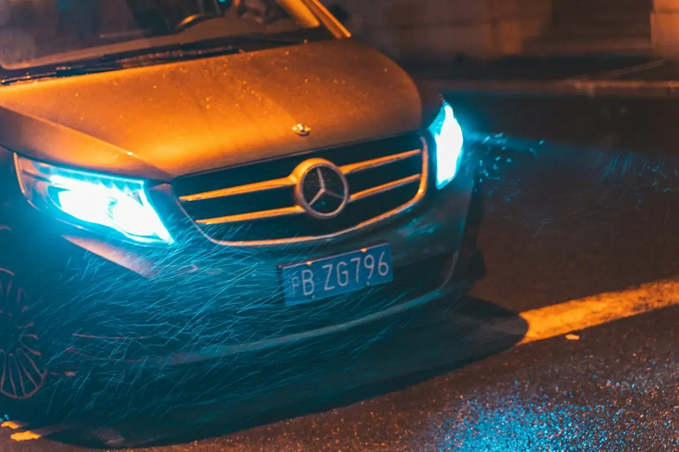 Calandre d'une Mercedes noire de nuit, phares allumés